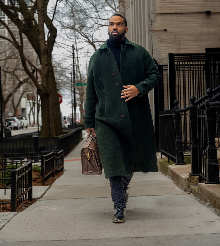 Menswear portrait in a green overcoat on a city sidewalk